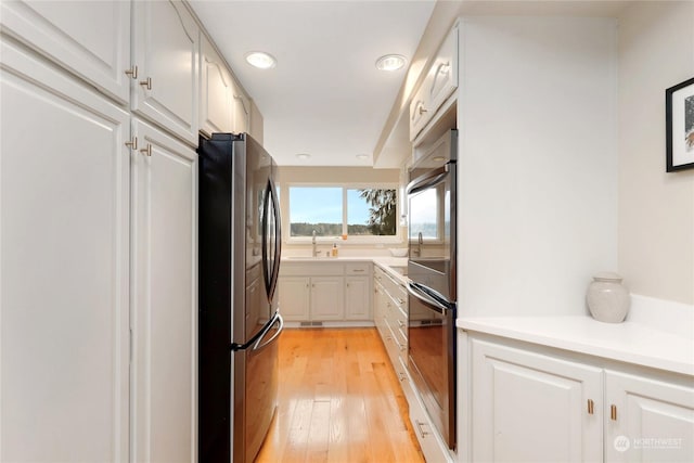 kitchen featuring white cabinets, double oven, light hardwood / wood-style floors, sink, and stainless steel refrigerator