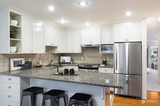 kitchen with a breakfast bar, stainless steel appliances, white cabinets, kitchen peninsula, and light wood-type flooring