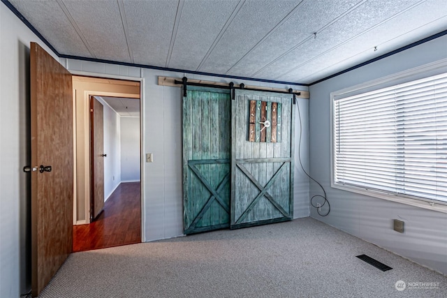 carpeted spare room featuring a barn door, crown molding, and a textured ceiling