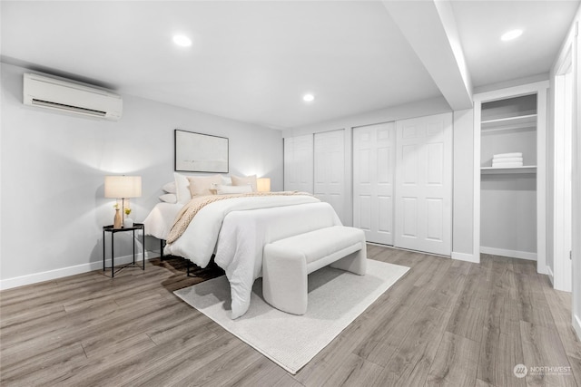 bedroom with an AC wall unit, light hardwood / wood-style flooring, and two closets