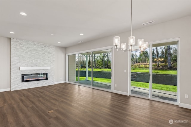 unfurnished living room featuring an inviting chandelier, a stone fireplace, and dark wood-type flooring