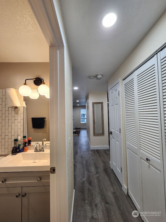 hallway with sink, dark wood-type flooring, and a textured ceiling