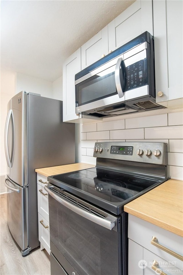 kitchen with stainless steel appliances, white cabinetry, tasteful backsplash, and light hardwood / wood-style floors