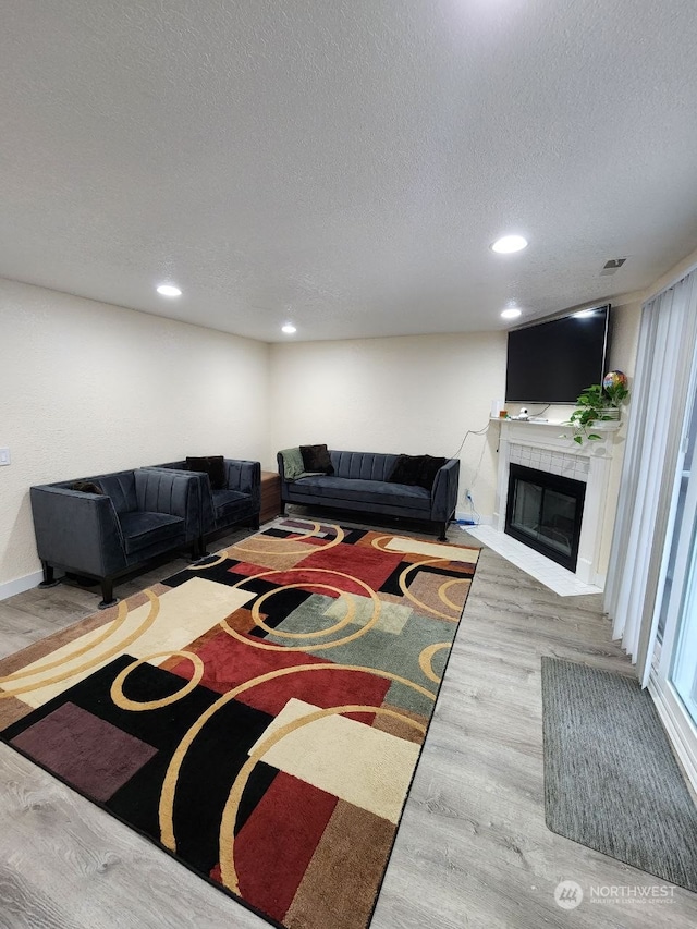 living room featuring a textured ceiling, hardwood / wood-style flooring, and a tiled fireplace