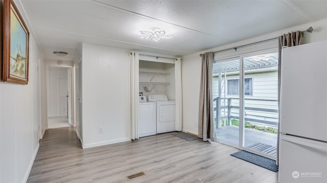 laundry room with independent washer and dryer, light wood-type flooring, and a textured ceiling