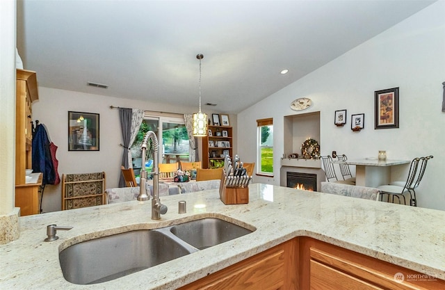 kitchen featuring decorative light fixtures, light stone counters, lofted ceiling, and sink