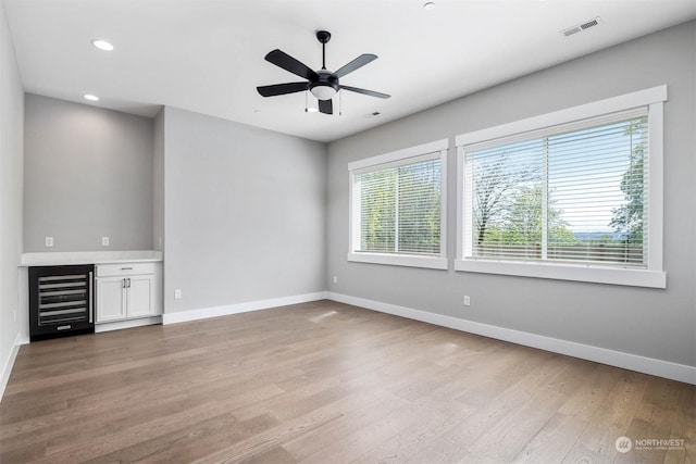 unfurnished living room featuring wine cooler, ceiling fan, and light hardwood / wood-style floors