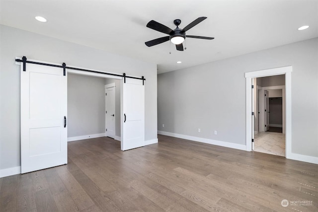 unfurnished bedroom featuring a barn door, ceiling fan, ensuite bathroom, and hardwood / wood-style flooring