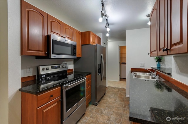 kitchen featuring sink, washer / clothes dryer, dark stone counters, track lighting, and appliances with stainless steel finishes