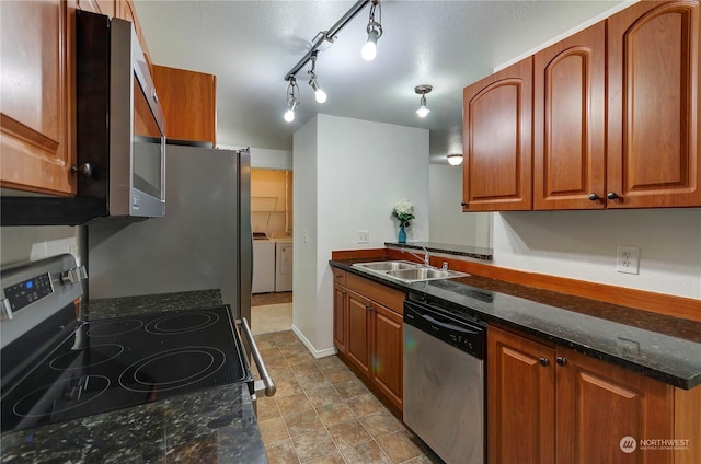 kitchen with appliances with stainless steel finishes, washer and clothes dryer, dark stone counters, and sink