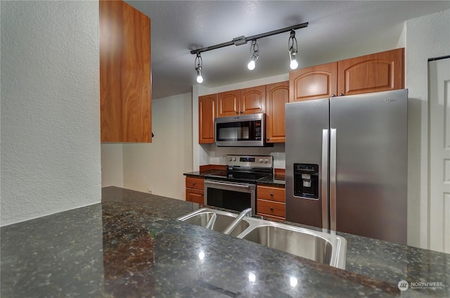 kitchen with stainless steel appliances, track lighting, dark stone counters, and sink