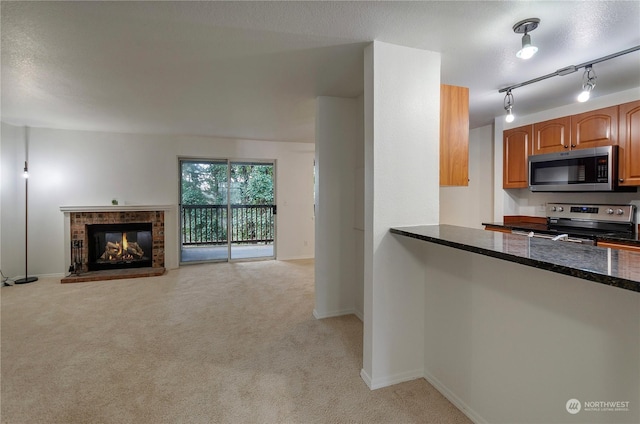 kitchen with a multi sided fireplace, light colored carpet, dark stone counters, a textured ceiling, and appliances with stainless steel finishes