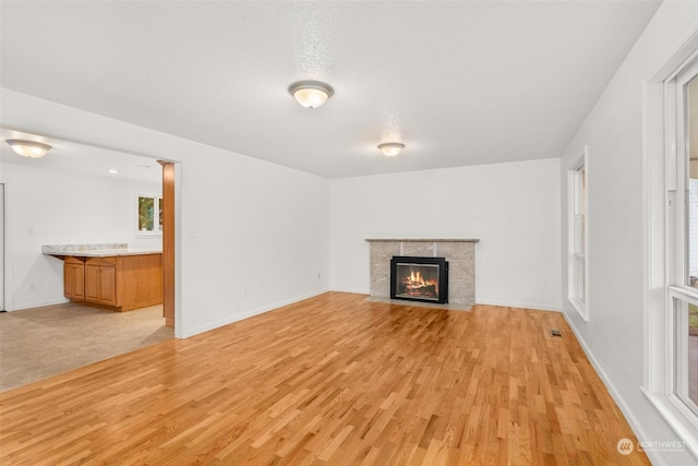 unfurnished living room with a textured ceiling, light hardwood / wood-style flooring, and a tiled fireplace