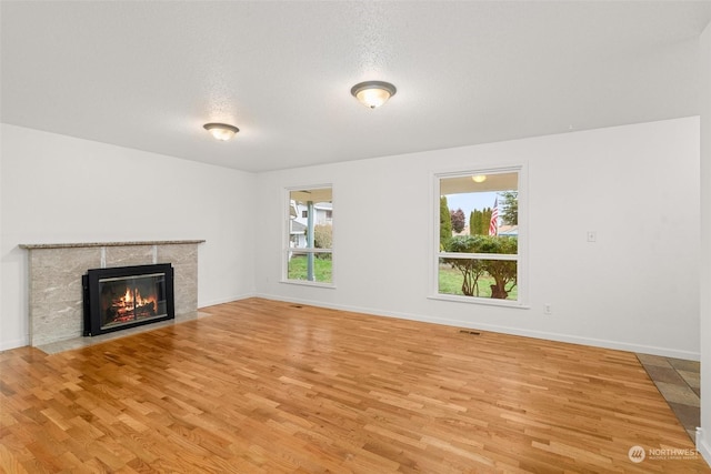 unfurnished living room featuring a tile fireplace, a textured ceiling, light wood-type flooring, and a healthy amount of sunlight