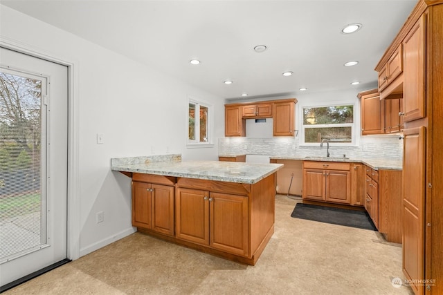 kitchen featuring kitchen peninsula, light stone counters, a wealth of natural light, and sink