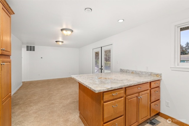 kitchen with plenty of natural light, light colored carpet, kitchen peninsula, and light stone counters