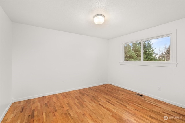 spare room with a textured ceiling and light hardwood / wood-style flooring