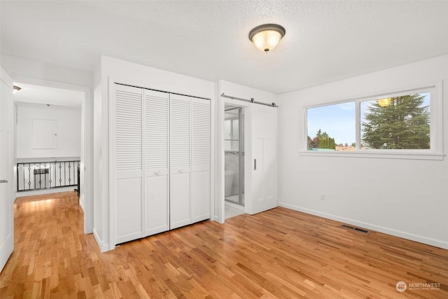 unfurnished bedroom featuring ensuite bath, a barn door, light hardwood / wood-style flooring, a textured ceiling, and a closet