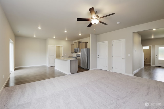 kitchen featuring light stone countertops, ceiling fan, a kitchen island with sink, dark carpet, and appliances with stainless steel finishes