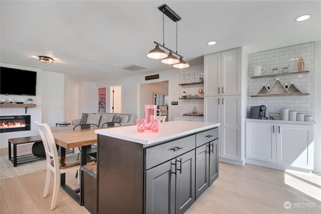 kitchen with gray cabinets, decorative backsplash, a kitchen island, and decorative light fixtures