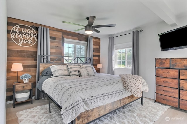 bedroom featuring hardwood / wood-style floors, beam ceiling, ceiling fan, and wood walls