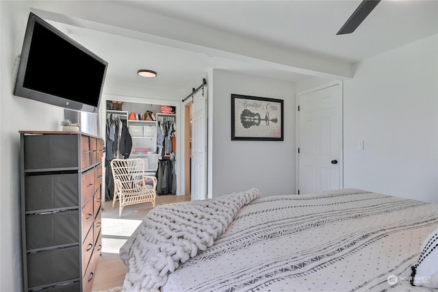 bedroom featuring a barn door, light hardwood / wood-style floors, a closet, and ceiling fan