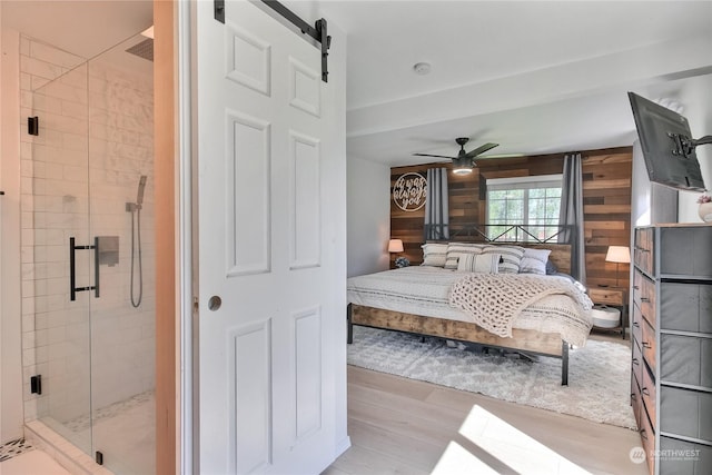 bedroom with a barn door, wooden walls, ceiling fan, and light wood-type flooring