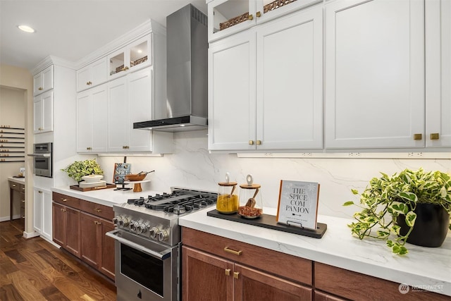 kitchen with wall chimney exhaust hood, glass insert cabinets, appliances with stainless steel finishes, dark wood-type flooring, and backsplash