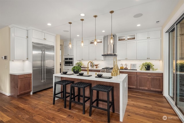 kitchen with dark wood finished floors, a breakfast bar, stainless steel appliances, light countertops, and wall chimney range hood