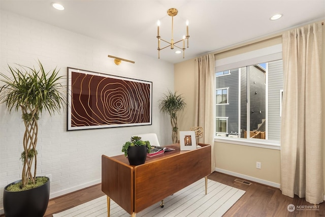 office featuring an inviting chandelier, visible vents, brick wall, and wood finished floors