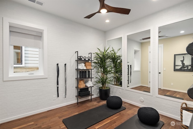 exercise area with baseboards, visible vents, a ceiling fan, brick wall, and wood finished floors