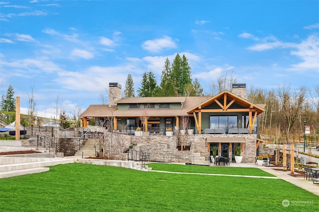 rear view of house with a lawn, a balcony, stone siding, a chimney, and a patio area