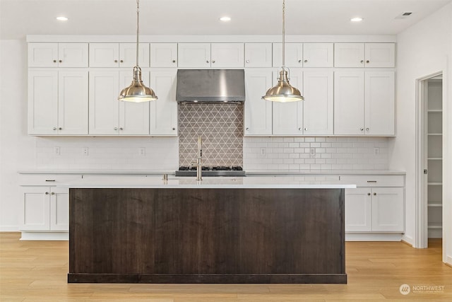 kitchen with pendant lighting, white cabinetry, and wall chimney exhaust hood