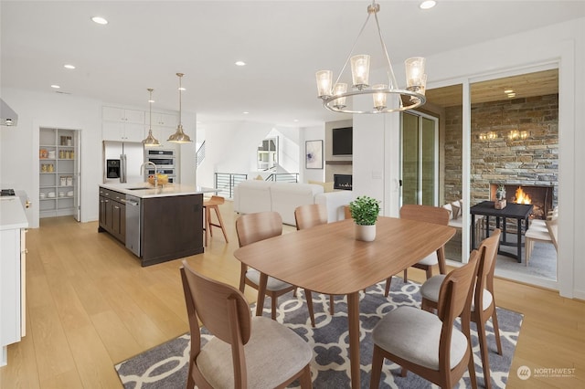 dining area with light hardwood / wood-style floors, a stone fireplace, sink, and a chandelier