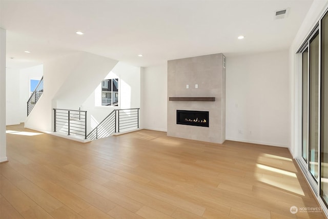 unfurnished living room with light wood-type flooring and a tiled fireplace