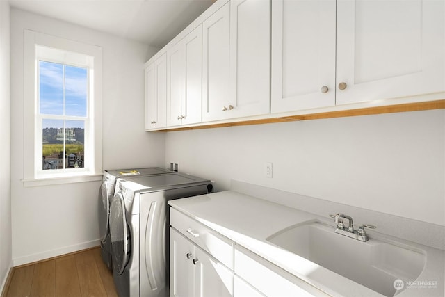 laundry room featuring washer and dryer, sink, cabinets, and wood-type flooring