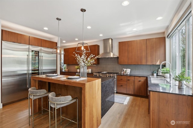 kitchen featuring pendant lighting, high end appliances, light hardwood / wood-style flooring, wall chimney exhaust hood, and a kitchen island