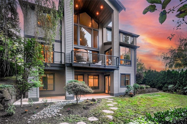 back house at dusk with a balcony and a lawn