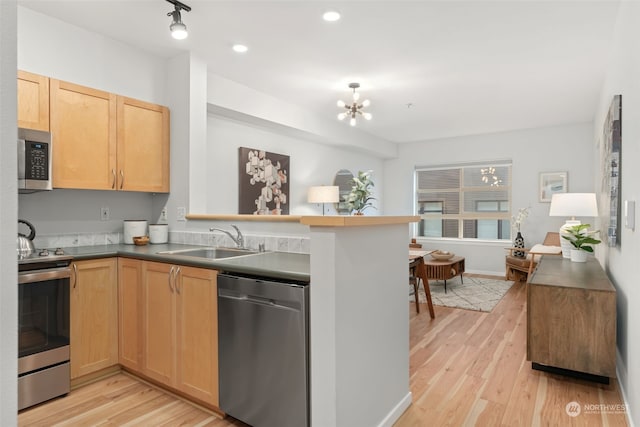 kitchen featuring kitchen peninsula, appliances with stainless steel finishes, light wood-type flooring, sink, and a chandelier