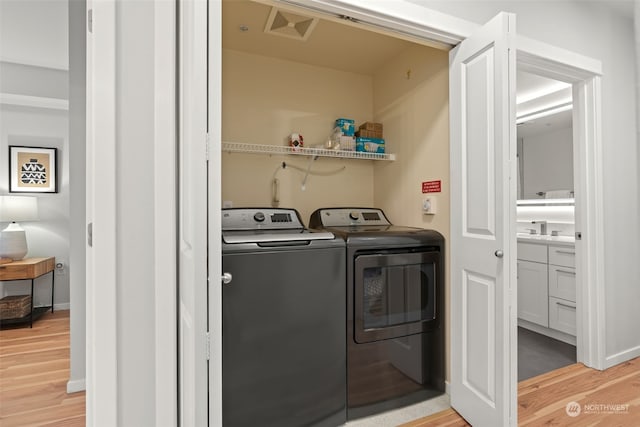 laundry area featuring washing machine and dryer, sink, and light wood-type flooring