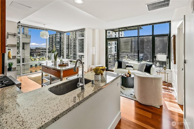 kitchen with sink, light stone counters, expansive windows, pendant lighting, and hardwood / wood-style flooring