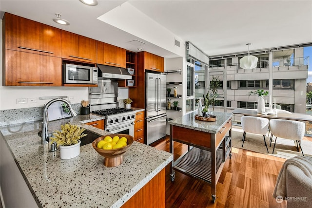 kitchen featuring sink, stainless steel appliances, light stone counters, hardwood / wood-style floors, and decorative light fixtures