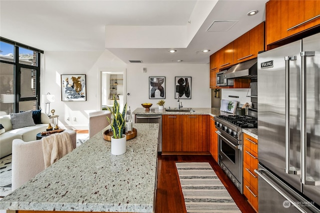 kitchen with light stone countertops, sink, a center island, a wall of windows, and premium appliances