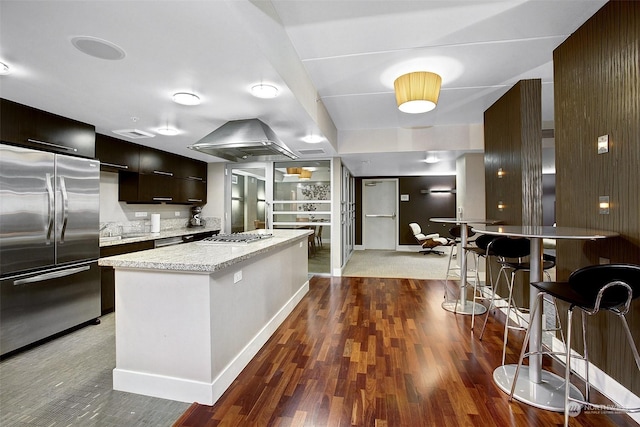 kitchen featuring light stone countertops, dark hardwood / wood-style floors, island range hood, a kitchen island, and appliances with stainless steel finishes