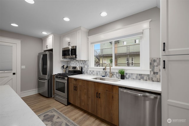 kitchen featuring white cabinets, sink, light hardwood / wood-style flooring, decorative backsplash, and stainless steel appliances