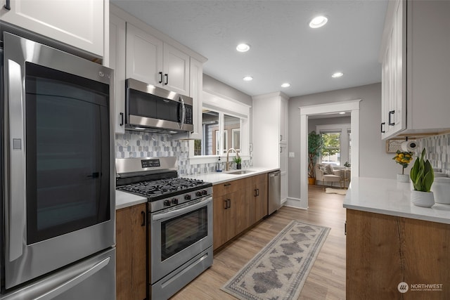 kitchen featuring white cabinets, sink, light wood-type flooring, tasteful backsplash, and stainless steel appliances