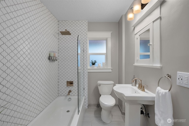 bathroom with a textured ceiling, tile patterned floors, tiled shower / bath combo, and toilet