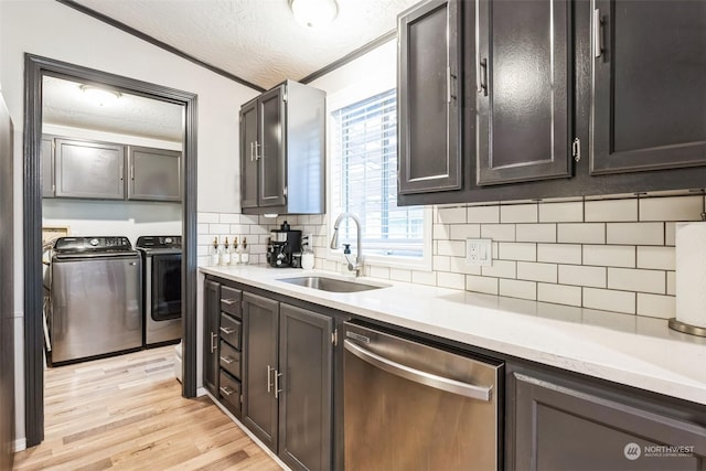 kitchen featuring sink, stainless steel dishwasher, washing machine and dryer, light wood-type flooring, and a textured ceiling