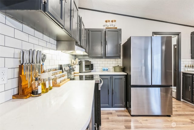 kitchen featuring backsplash, stainless steel refrigerator, light hardwood / wood-style flooring, and lofted ceiling