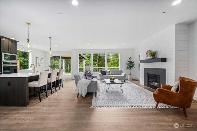 living room featuring light wood-type flooring, sink, and a tiled fireplace